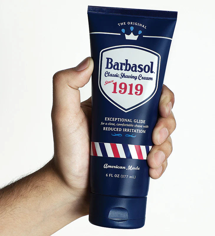 A hand holding a tube of Barbasol Classic Shaving Cream with the label '1919' prominently displayed, indicating the brand's year of invention.
