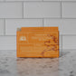 Orange soap packaging with text on a gray tiled background
