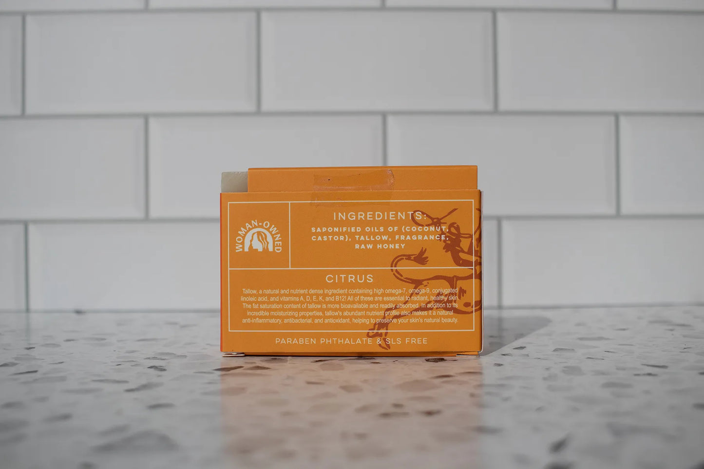 Orange soap packaging with text on a gray tiled background