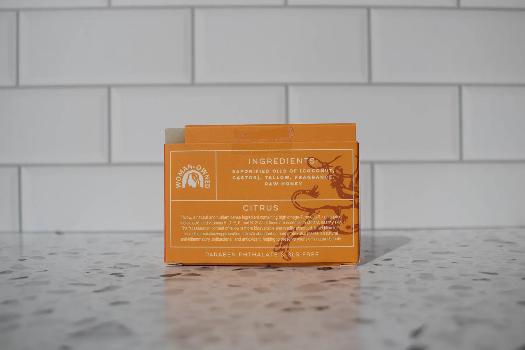 Orange soap packaging with text on a gray tiled background
