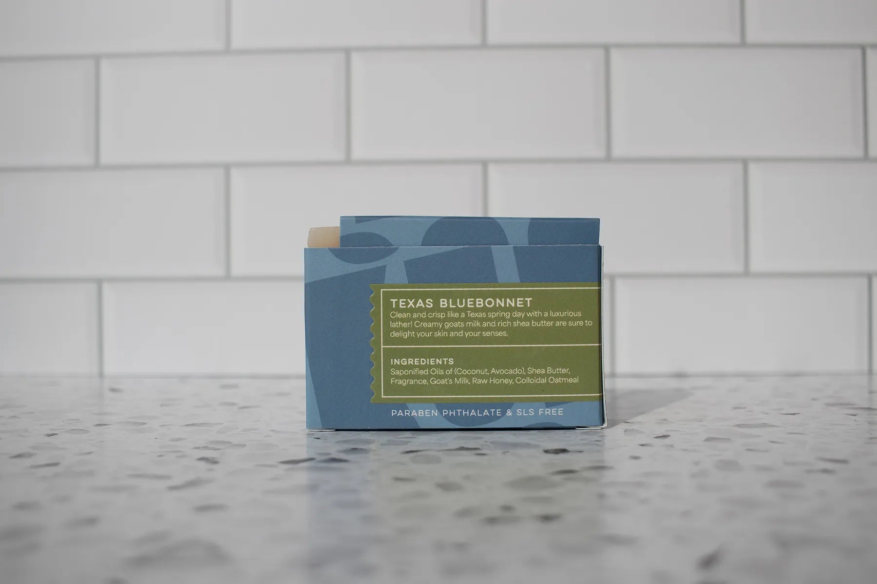 Bar of soap with a label on a marble surface against a tiled wall background